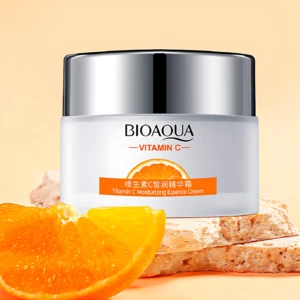Crema Bioaqua Vitamina C en tarro blanco con tapa plateada, acompañada de rodaja de naranja y rebanadas de pan sobre fondo beige.