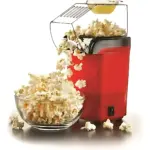 Crispetera eléctrica roja de aire caliente expulsando palomitas hacia un bol de vidrio transparente sobre una mesa.