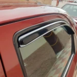 Deflector de ventana para auto en color rojo, instalado en la puerta lateral. Incluye goma flexible negra que sella el borde superior del cristal, permitiendo ventilación sin entrada de lluvia o viento.
