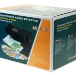 Caja del detector de billetes falsos AD-2138, con luz UV y lupa integrada, mostrando billetes de euro en su interior.