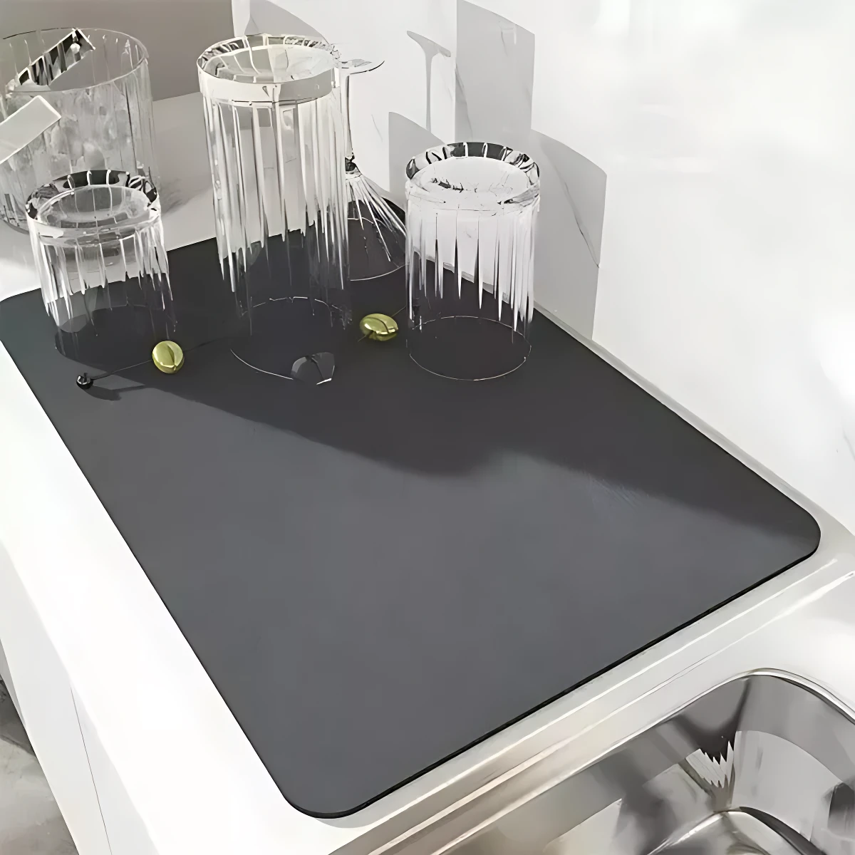 Tapete absorbente negro rectangular en cocina, con vasos de vidrio y limones sobre su superficie, colocado junto al fregadero.
