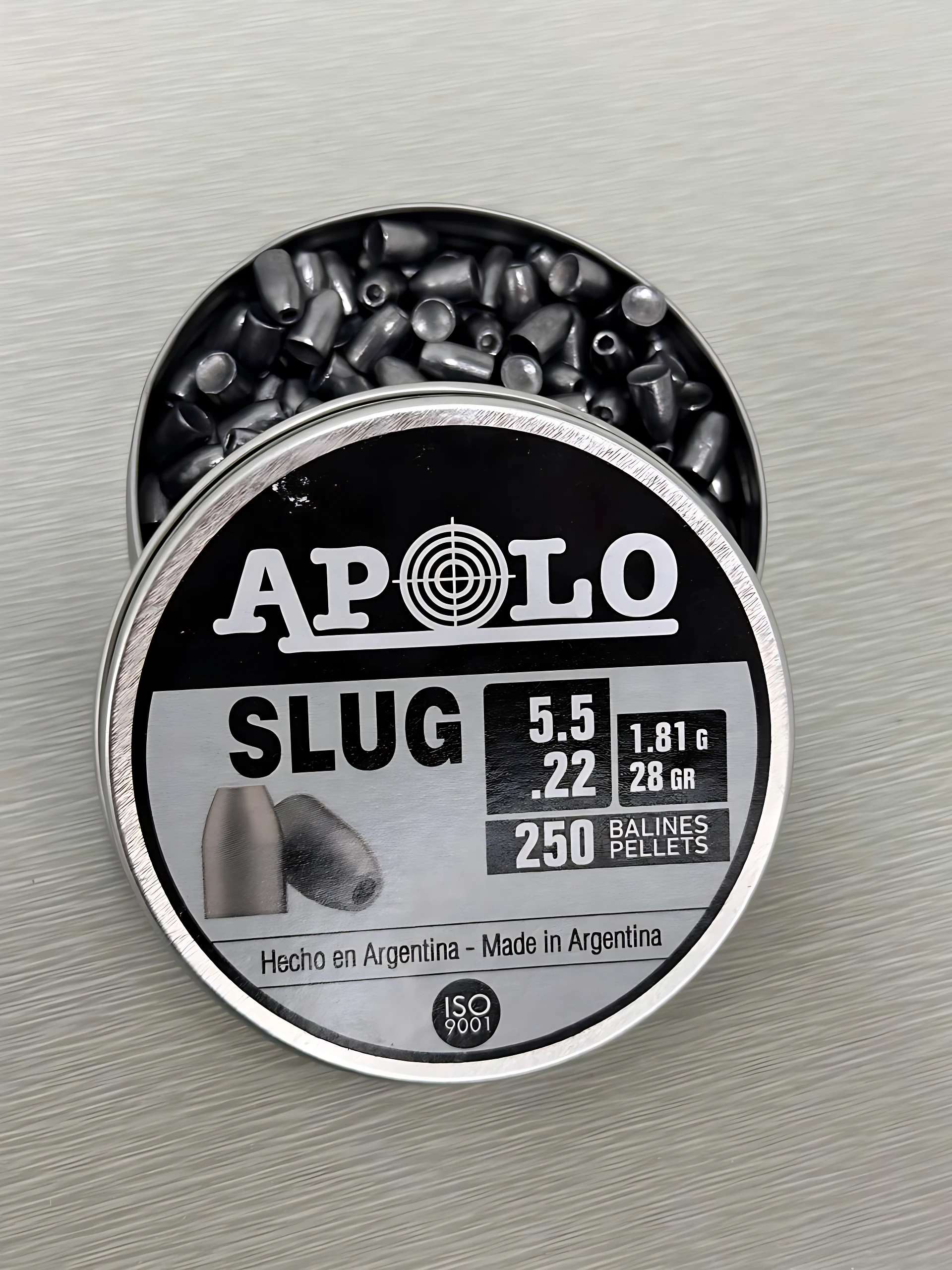 Lata abierta de perdigones Apolo Slug 5.5 mm calibre .22 de 28 grains, mostrando múltiples balines de plomo en su interior y la etiqueta con especificaciones.