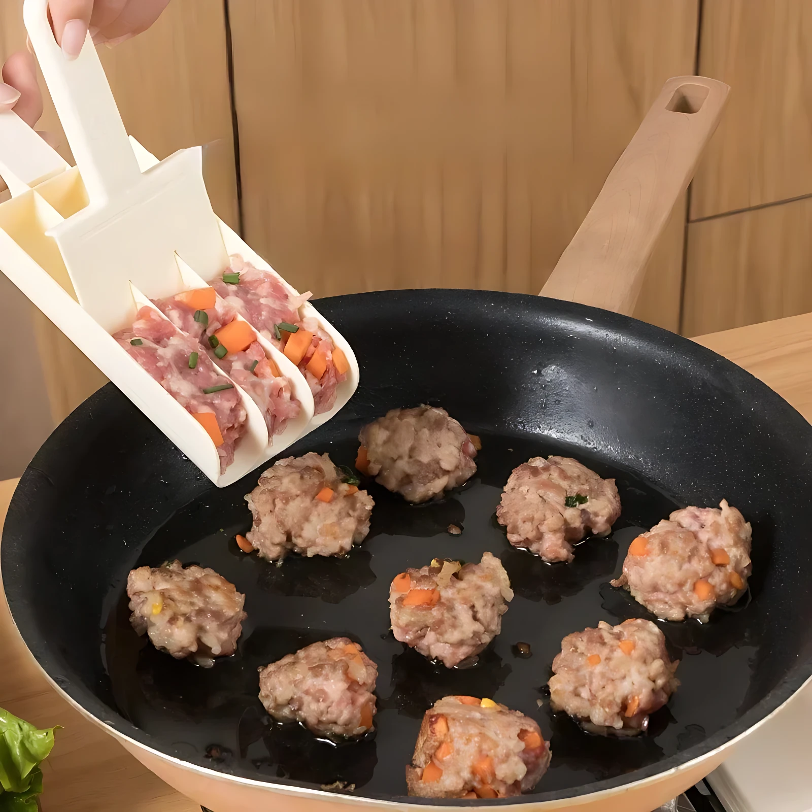 Dispensador de albóndigas en uso, depositando porciones de carne con vegetales en sartén negra sobre superficie de madera.
