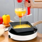 Dispensador de masa con medidor de porciones, vierte huevo batido en sartén cuadrada sobre base calefactora, con mango rojo y escala visible en mililitros.