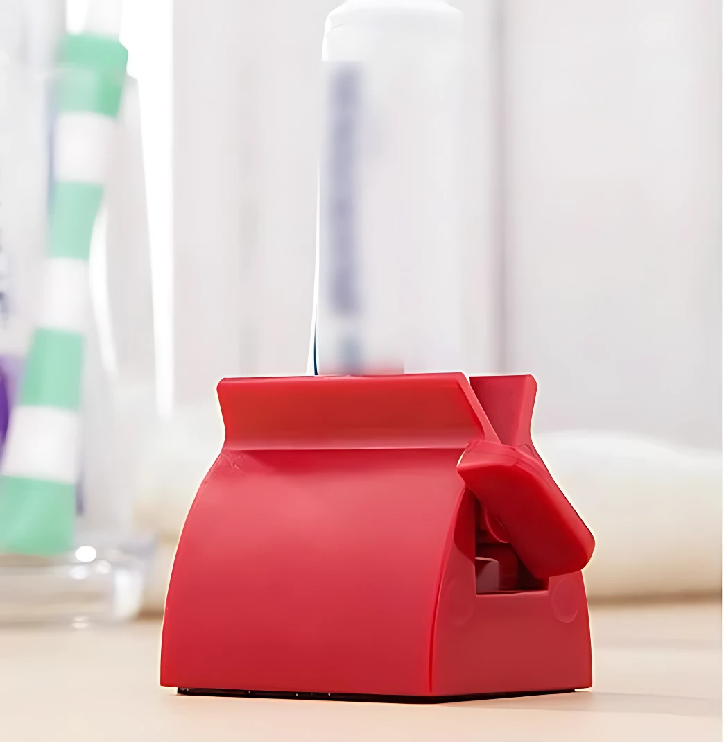 Dispensador manual de crema dental en color rojo, con forma de casa y mango ergonómico, diseñado para vaciar tubos de pasta de dientes de manera eficiente.