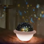 Proyector de cielo estrellado con cúpula negra y base blanca, proyectando estrellas y lunas sobre pared y suelo.