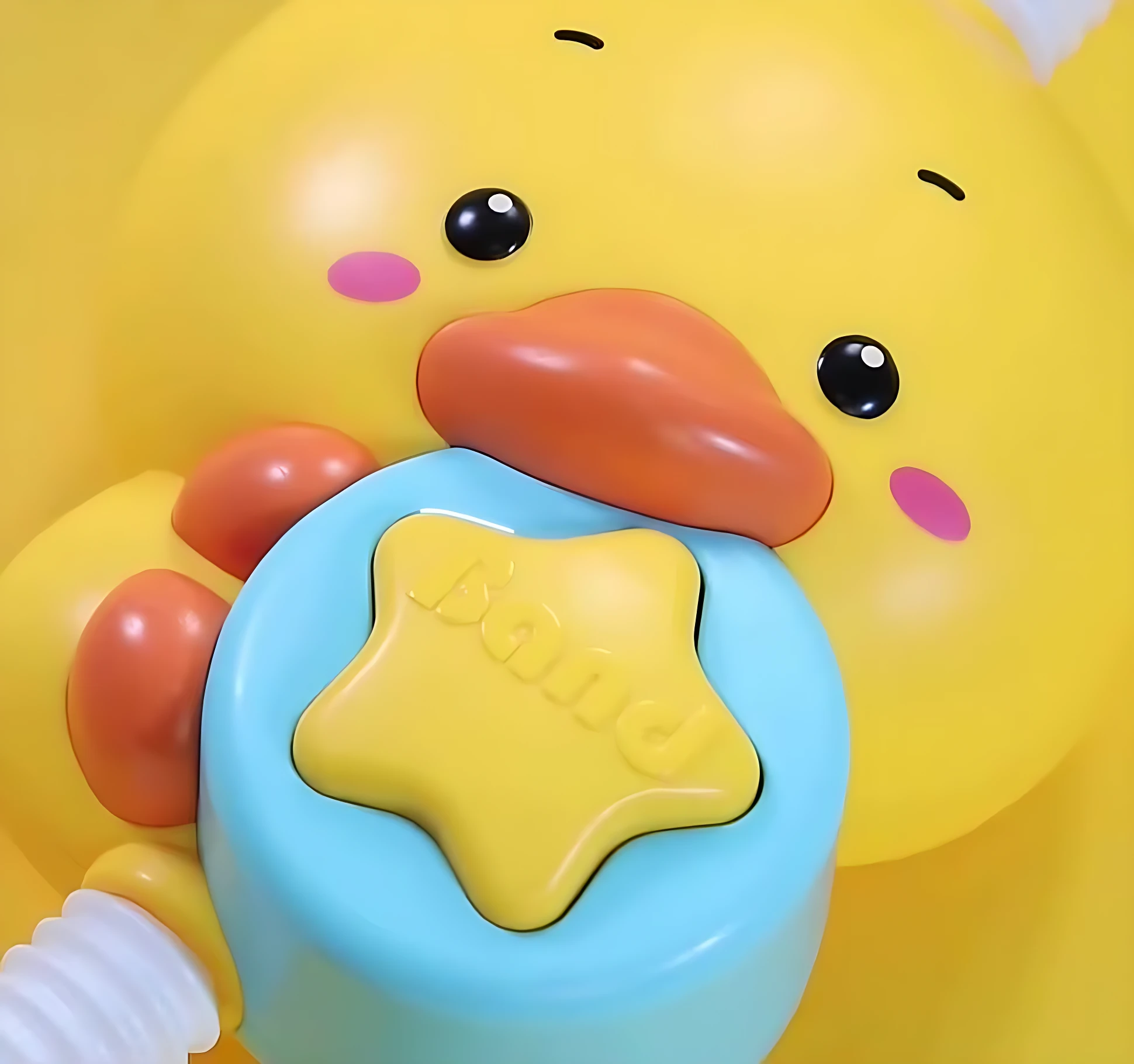 Ducha eléctrica de pato amarillo con pico naranja y botón azul estrellado; accionada manualmente para calmar al bebé durante el baño.