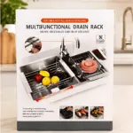 Escurridor de platos ajustable para fregadero, con rejilla metálica y soporte para frutas y verduras, sobre encimera blanca en cocina moderna.
