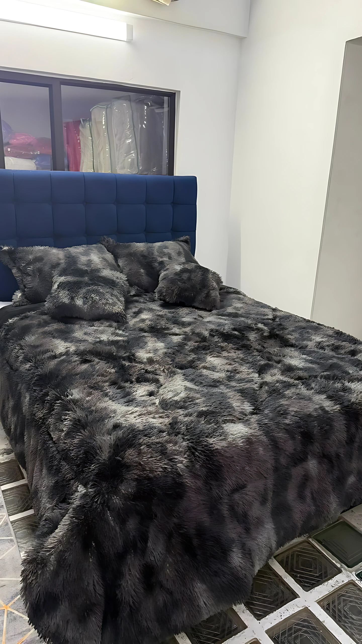 Edredón térmico peludo negro sobre cama doble con cabecero azul tapizado, textura suave y voluminosa en ambiente interior.