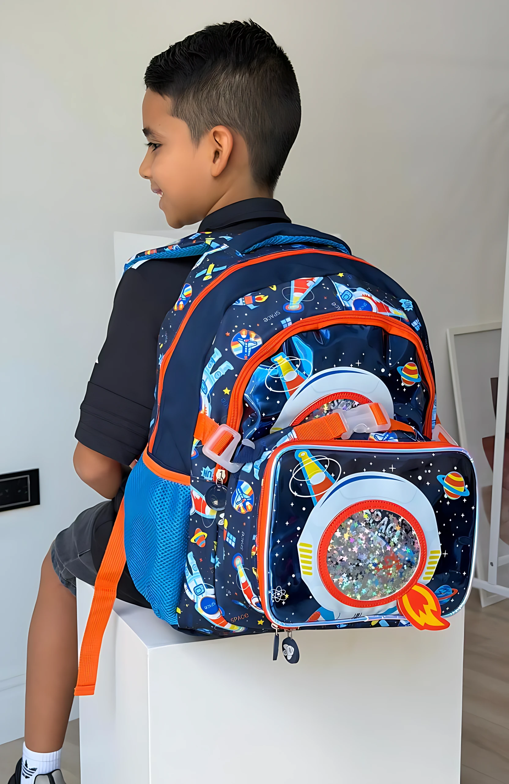 Morral escolar infantil azul espacial con lonchera térmica integrada, usado por niño sentado en caja blanca.