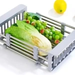 Escurridor de acero inoxidable con rejilla, color gris claro, mostrando vegetales frescos y frutas sobre su superficie.