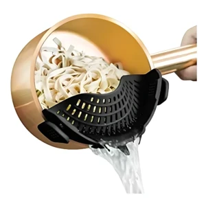 Escurridor de pasta negro con soporte para olla, en uso sobre recipiente dorado con fideos y agua escurriéndose.