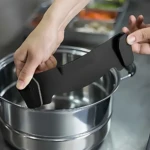 Escurridor de pasta negro con soporte para olla, siendo colocado sobre recipiente metálico en cocina.