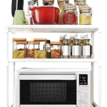 Estante blanco de tres niveles con horno microondas en la base, organizador de cocina con tarros de especias y utensilios en los estantes superiores.