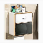 Dispensador de papel higiénico blanco con marco dorado, estante superior para accesorios de baño y cajón frontal.