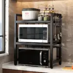 Estante negro de dos niveles para microondas, con estantería superior que incluye recipiente blanco y organizador de especias, y ganchos laterales para utensilios de cocina.