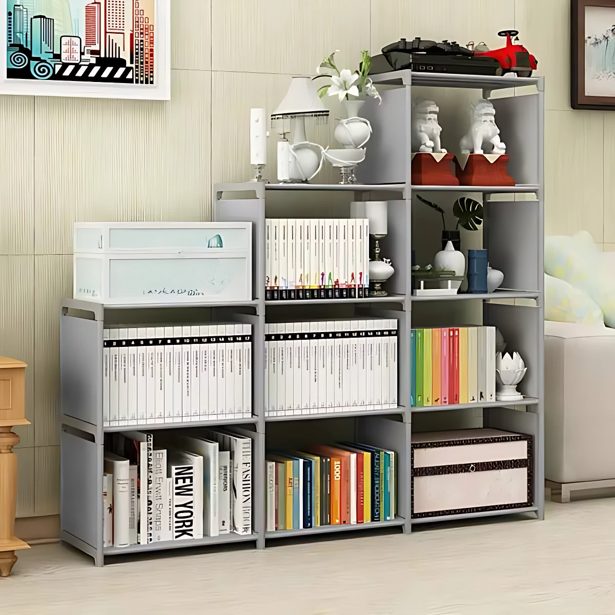 Estante organizador modular gris claro con cuatro niveles, exhibe libros, cajas de almacenamiento y objetos decorativos en un ambiente interior.