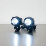 Dos faros LED auxiliares JRY-10 de 100W, color negro, montados sobre superficie gris, emitiendo luz blanca intensa.