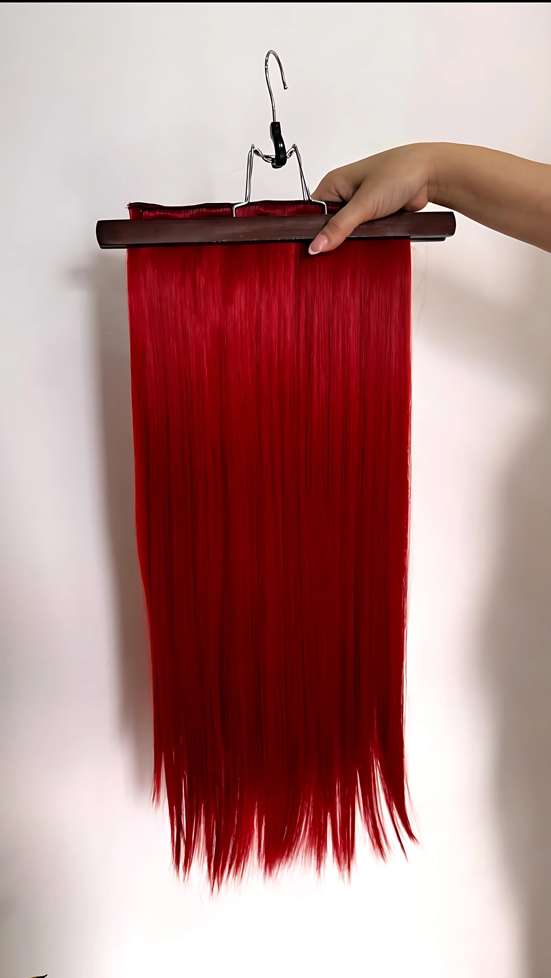 Extensiones de cabello semi humanas lisas con clips, color rojo intenso, presentadas colgadas en soporte de madera sobre fondo blanco.
