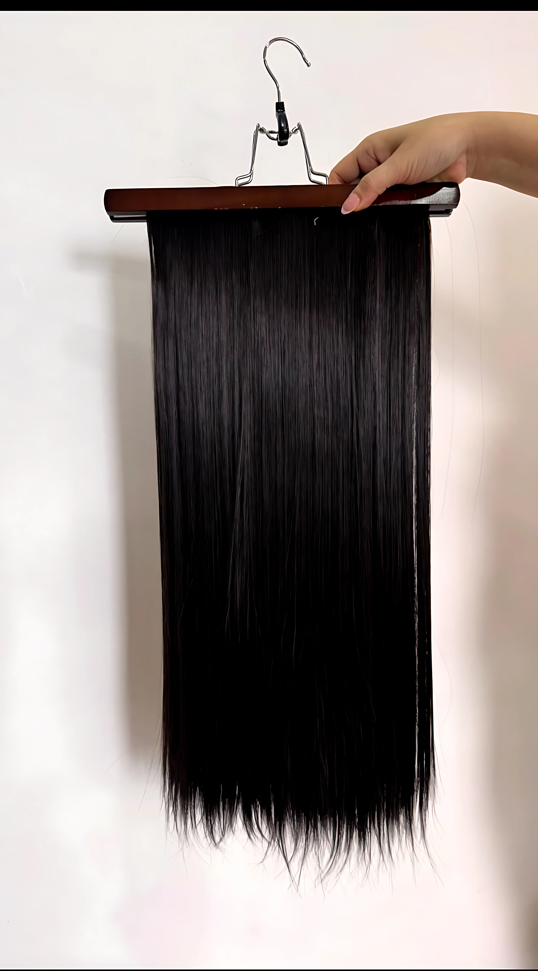 Extensiones de cabello semi humanas lisas con clips, color negro intenso, textura sedosa y caída recta, montadas en soporte de madera para exhibición.