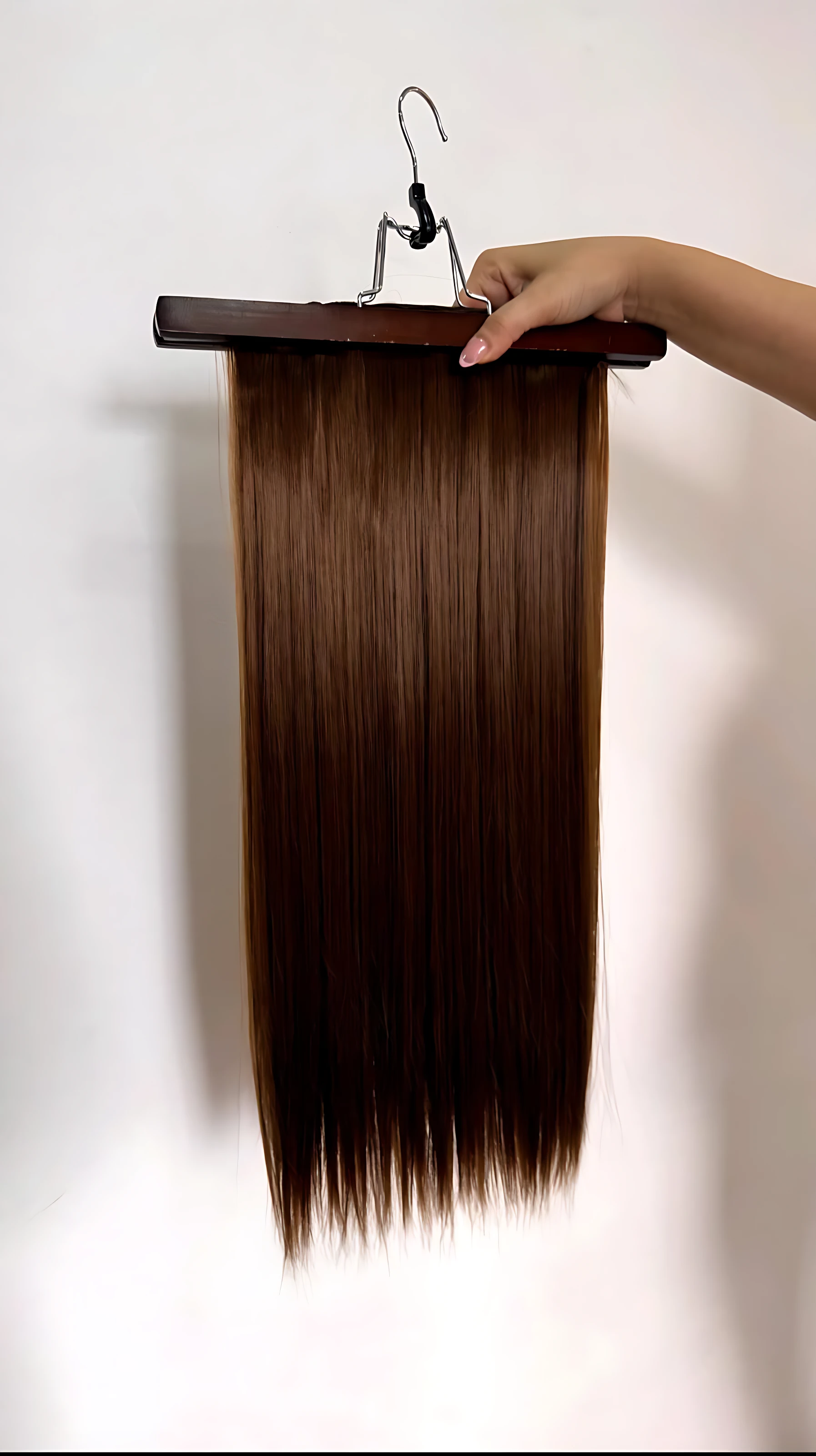 Extensiones de cabello semi humanas lisas con clips, color castaño oscuro, colgando de soporte de madera sobre fondo blanco.