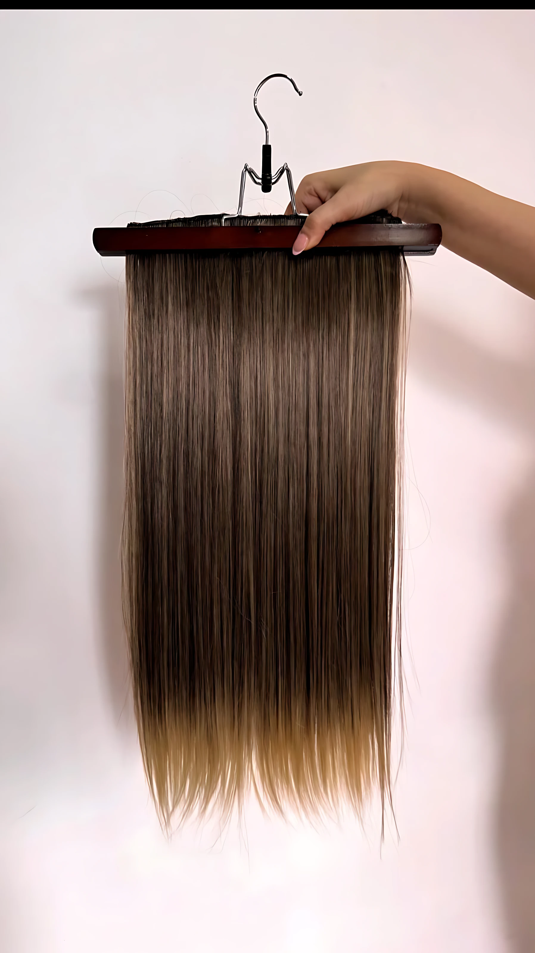 Extensiones de cabello semi humanas lisas con clips, color castaño con degradado a rubio, colgando de un perchero de madera.