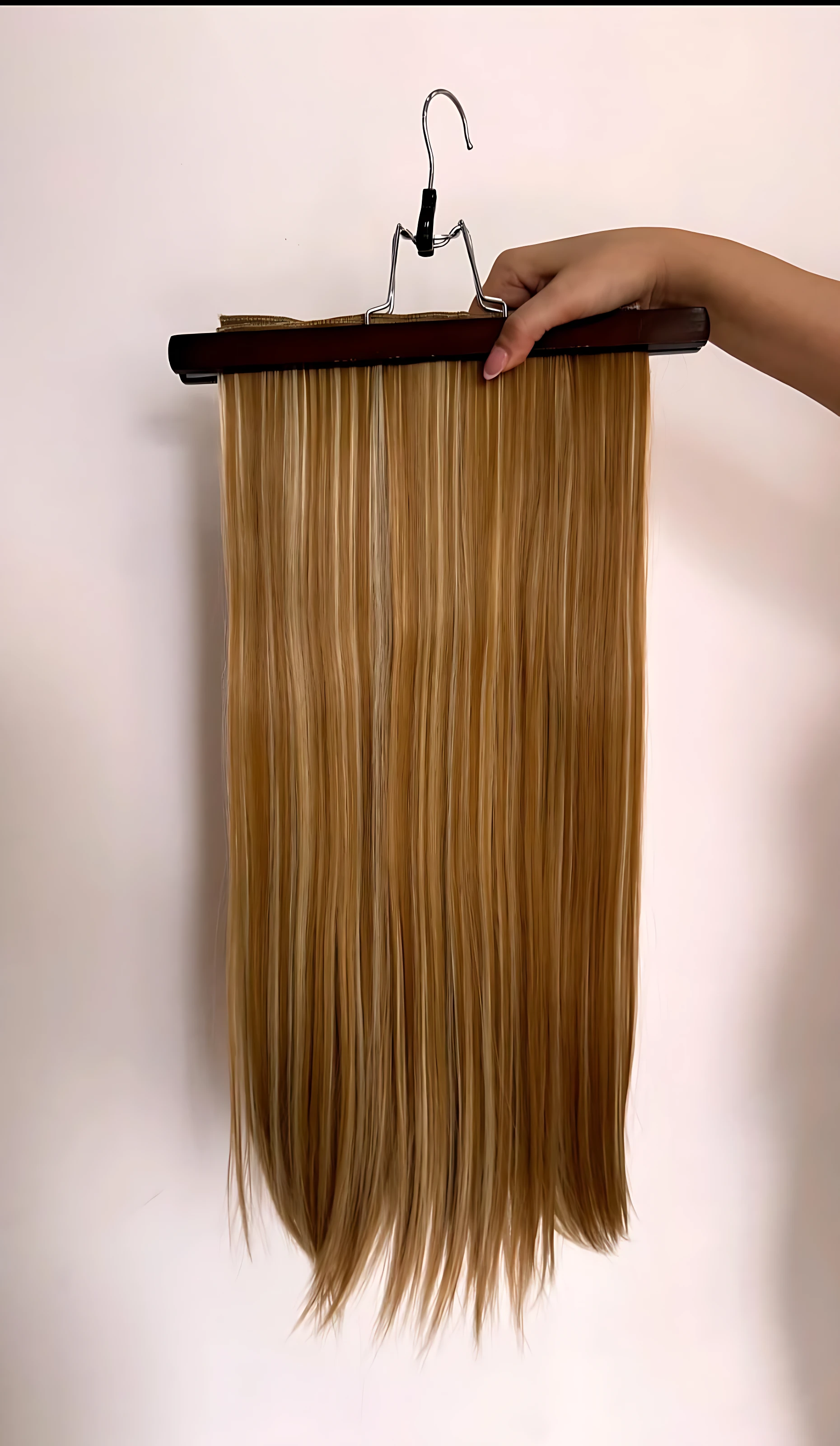 Extensiones de cabello semi humanas lisas con clips, color rubio miel, colgando de un perchero de madera.
