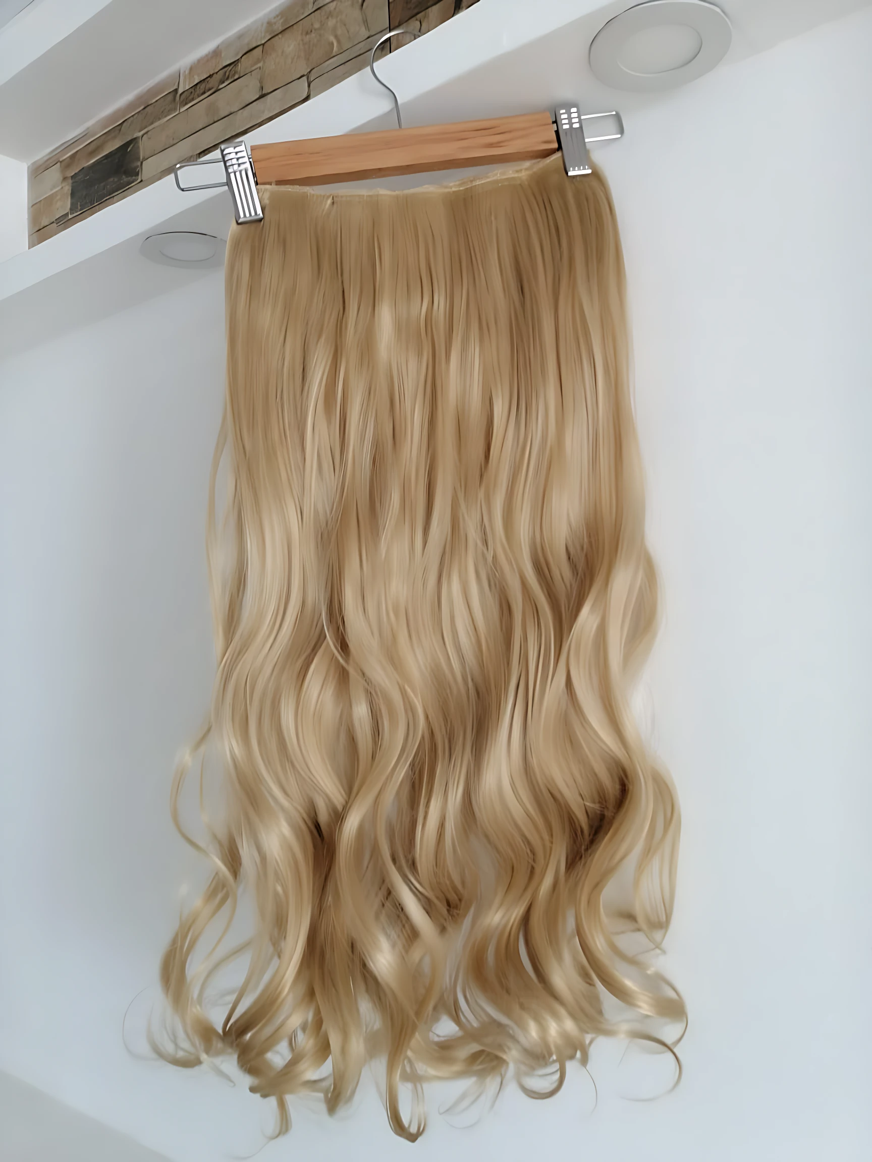 Extensiones semi humanas onduladas color rubio claro con clips metálicos, colgadas en perchero de madera.