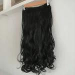 Extensiones semi humanas onduladas para clip, color negro, colgando de un perchero en interior.
