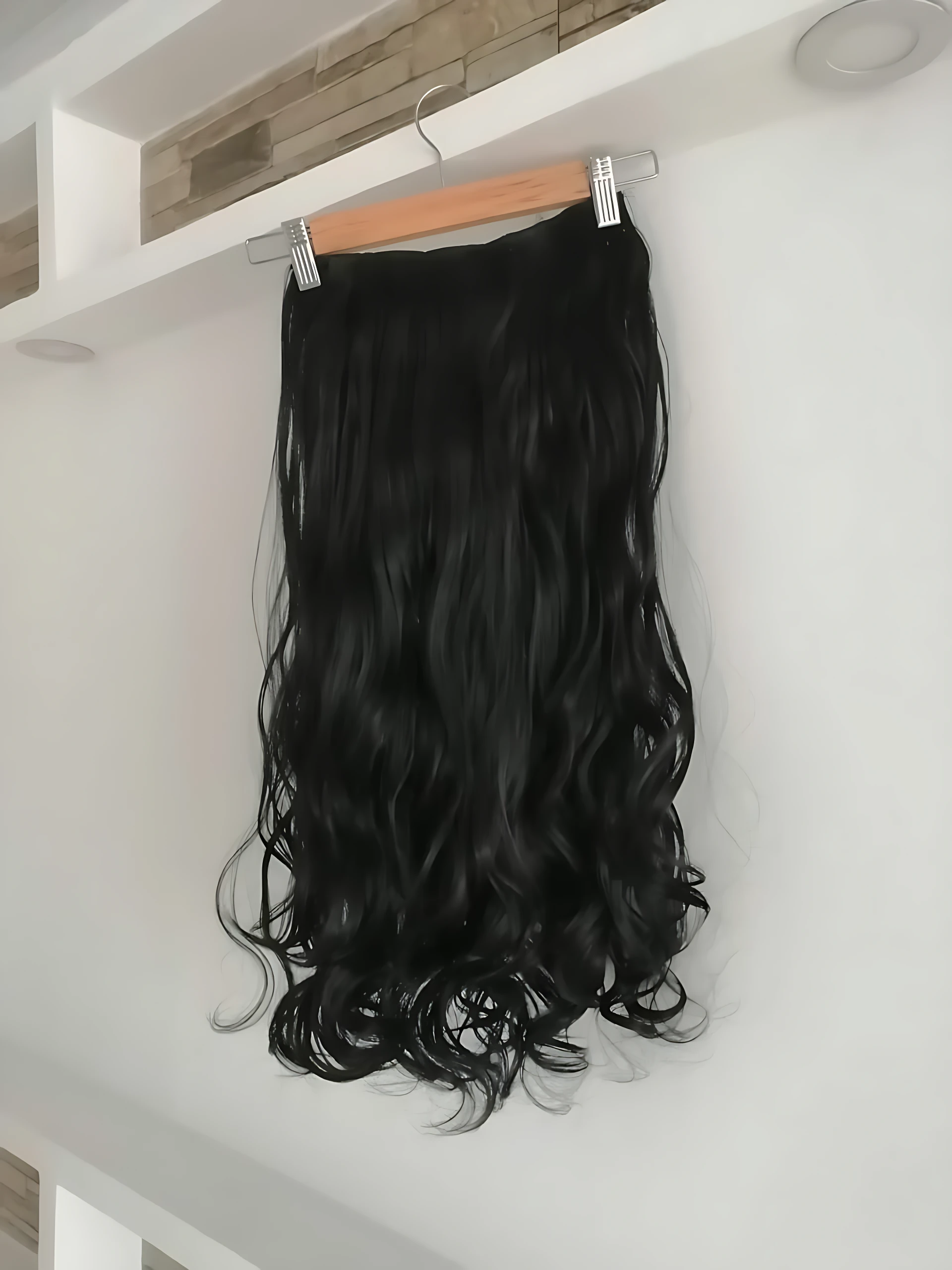 Extensiones semi humanas onduladas para clip, color negro, colgando de un perchero en interior.