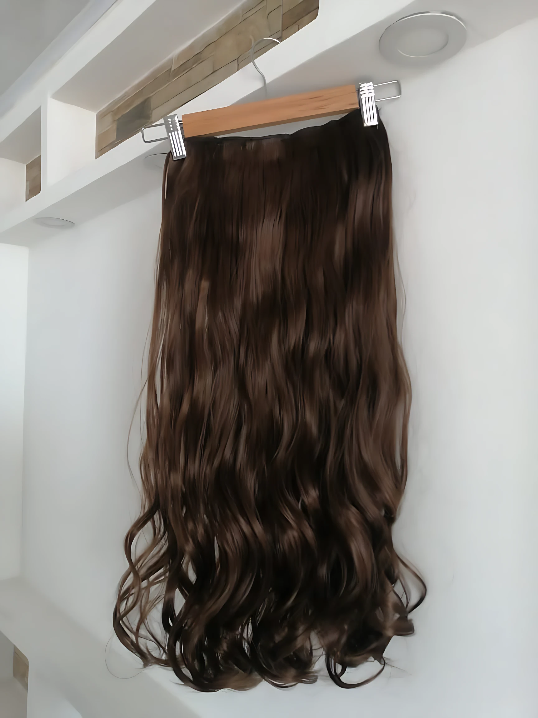 Extensiones semi humanas onduladas color castaño oscuro con clips metálicos, colgando sobre estante blanco.