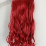 Extensiones semi humanas onduladas rojas con clips metálicos, colgadas en perchero de madera sobre fondo blanco.