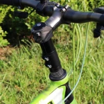 Extensor de manubrio de aluminio negro con cables verdes, instalado en bicicleta de color verde lima sobre césped.