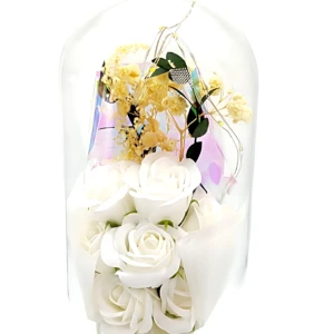 Domo de vidrio con arreglo floral eterno en blanco y amarillo, sobre base negra circular. Incluye rosa blanca, flores amarillas y hojas verdes, con detalles de cintas blancas. Medidas visibles: 21 cm de altura por 11 cm de ancho.
