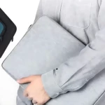 Funda para portátil 15.6 pulgadas en color gris claro con textura lino, siendo sostenida por una mano sobre el brazo de una persona.