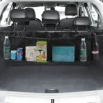 Organizador negro para baúl de camioneta con compartimentos, mostrando botellas, latas y cajas almacenadas tras los asientos traseros.