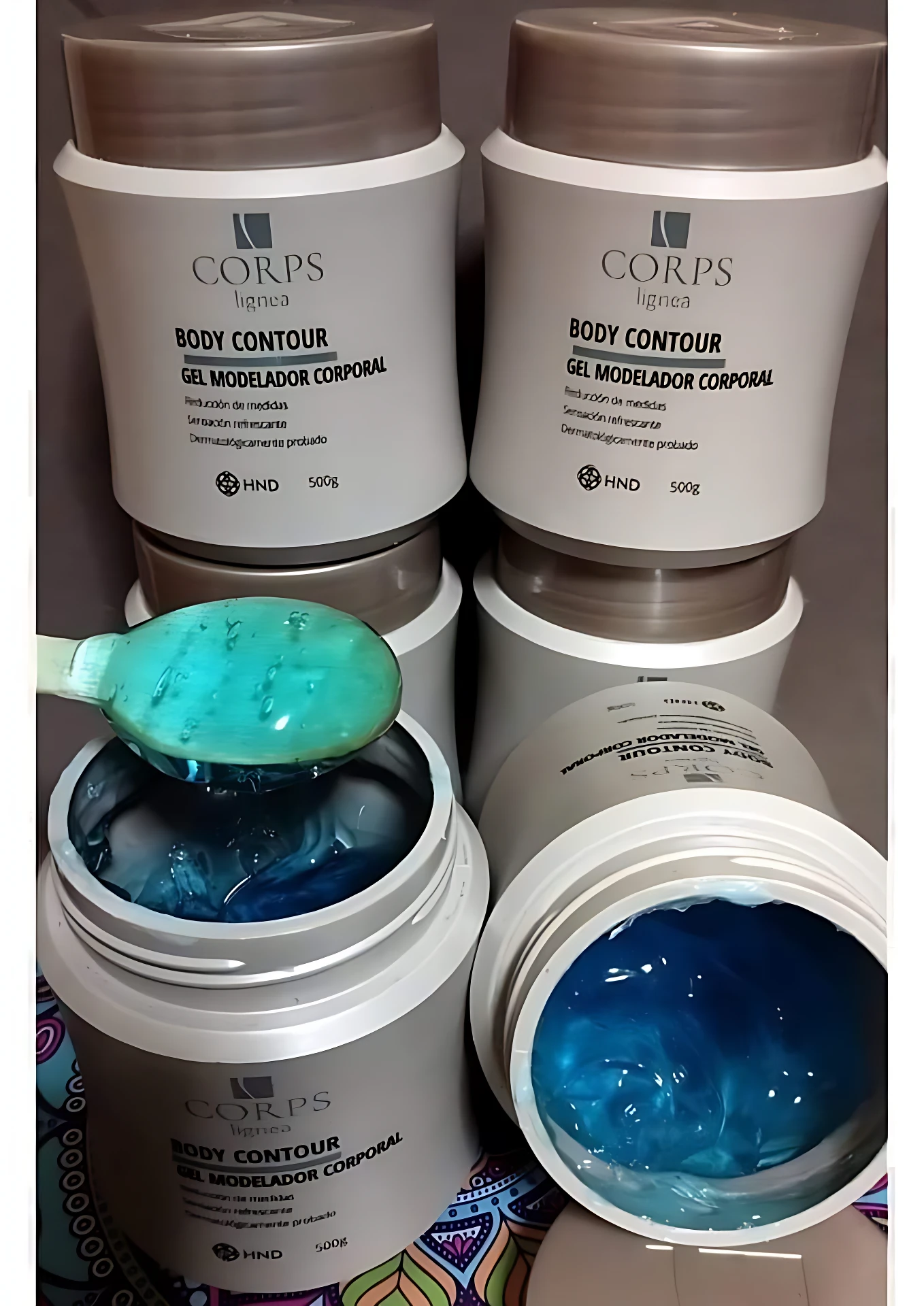 Cuatro frascos de gel moldeador corporal Corps Lignea en tonos beige y blanco, con tapa marrón; uno abierto mostrando textura azul brillante y espesa, otro con cuchara verde aplicando producto.