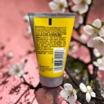 Tubo amarillo de gel para cabello Got2b con instrucciones visibles, sobre rama con flores blancas.