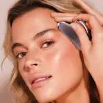 Mujer usando guasha facial de jade plateado en la frente, con acabado brillante y diseño ergonómico para masaje de drenaje linfático.