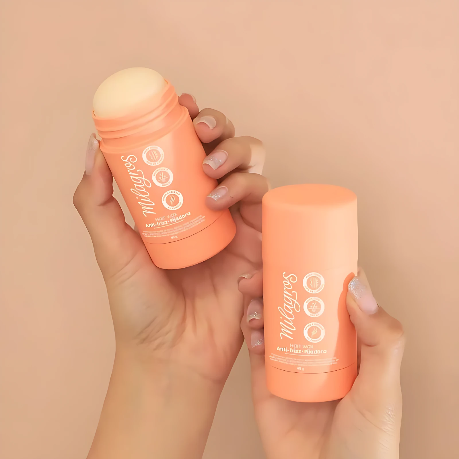 Dos manos sostienen dos presentaciones del producto: uno abierto mostrando la cera sólida de tono crema y otro cerrado con tapa naranja. Ambos tubos son de color coral con logotipo blanco y detalles circulares en la etiqueta frontal.