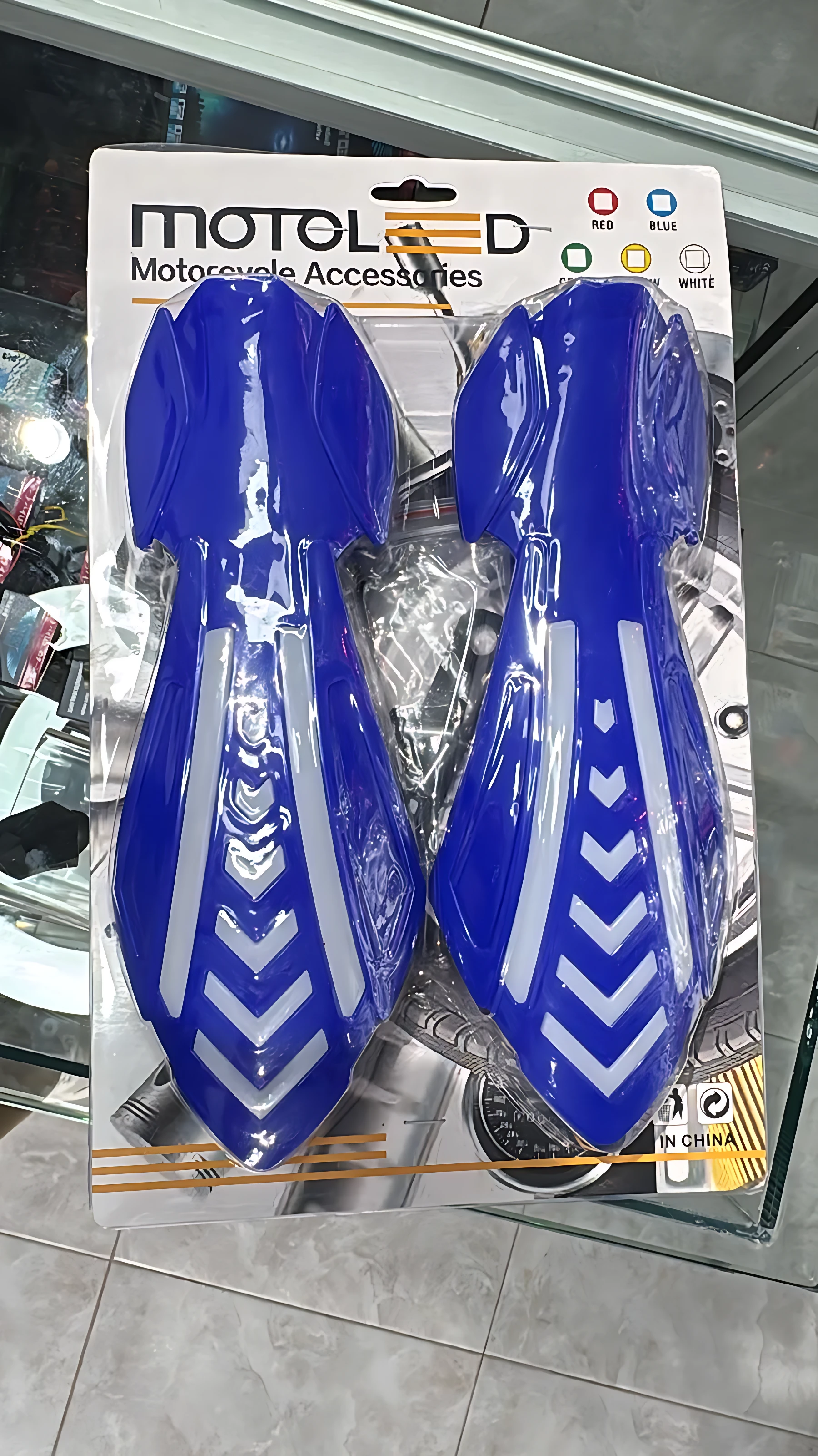 Cortavientos azul brillante con diseño de flechas blancas y luces LED integradas, presentado en empaque original de la marca MotoLED.