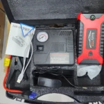 Iniciador de carro rojo y negro con power bank integrado, compresor de aire, cables de arranque, medidor de presión y accesorios en maleta de transporte.