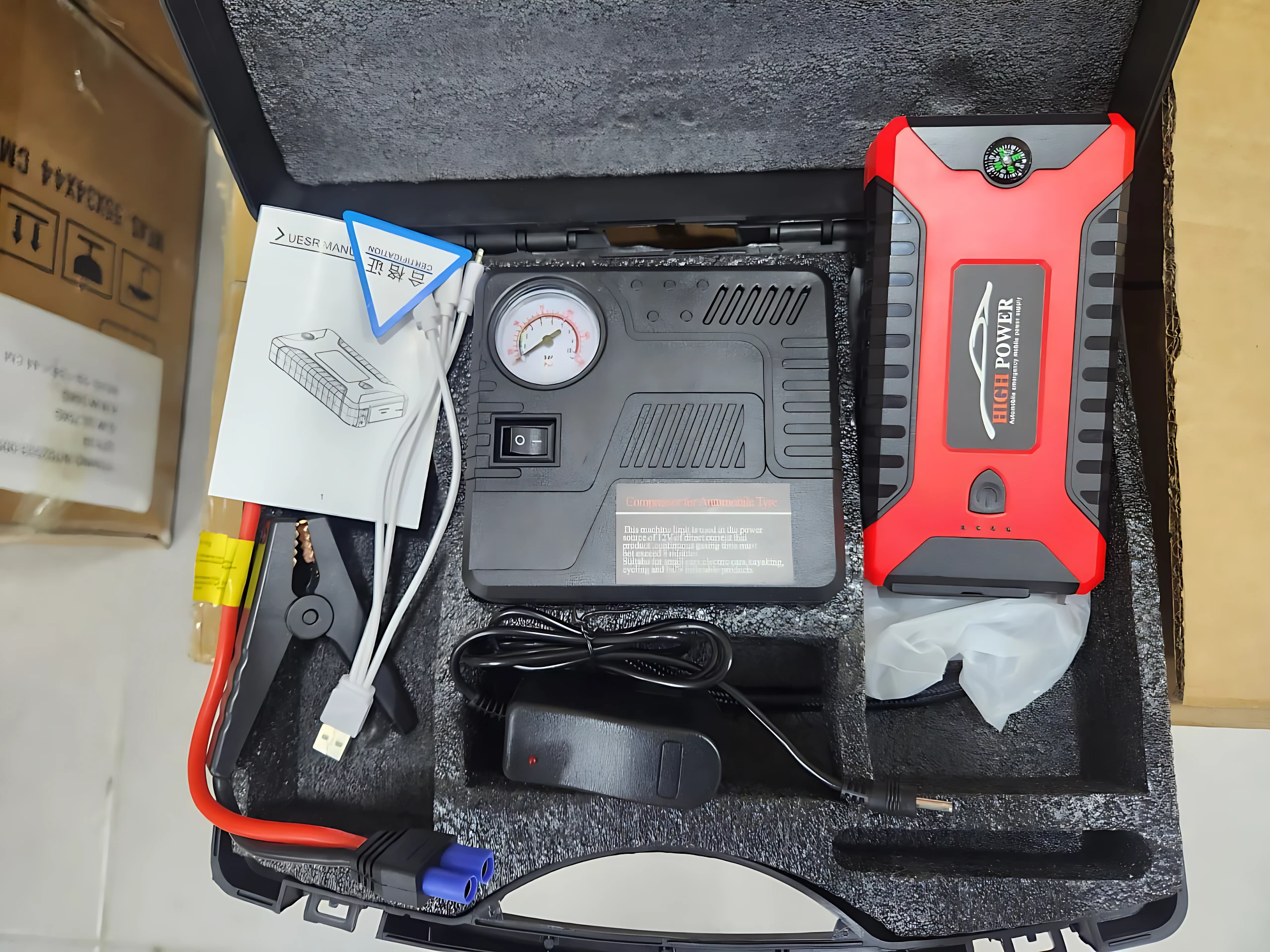 Iniciador de carro rojo y negro con power bank integrado, compresor de aire, cables de arranque, medidor de presión y accesorios en maleta de transporte.