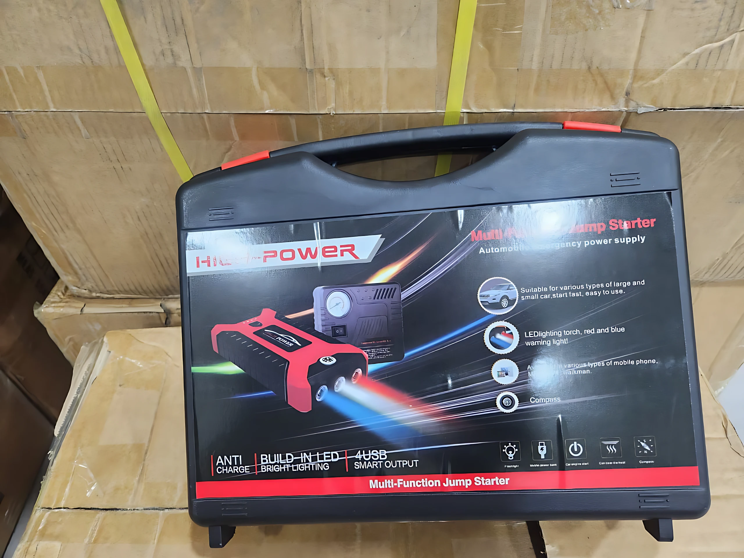 Iniciador de carro rojo en maleta negra con luces LED, puerto USB y compresor integrado para arrancar motores e inflar llantas.