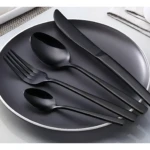 Juego de cubiertos negro mate sobre plato, incluye tenedor, cuchara y cuchillo, vista cenital.