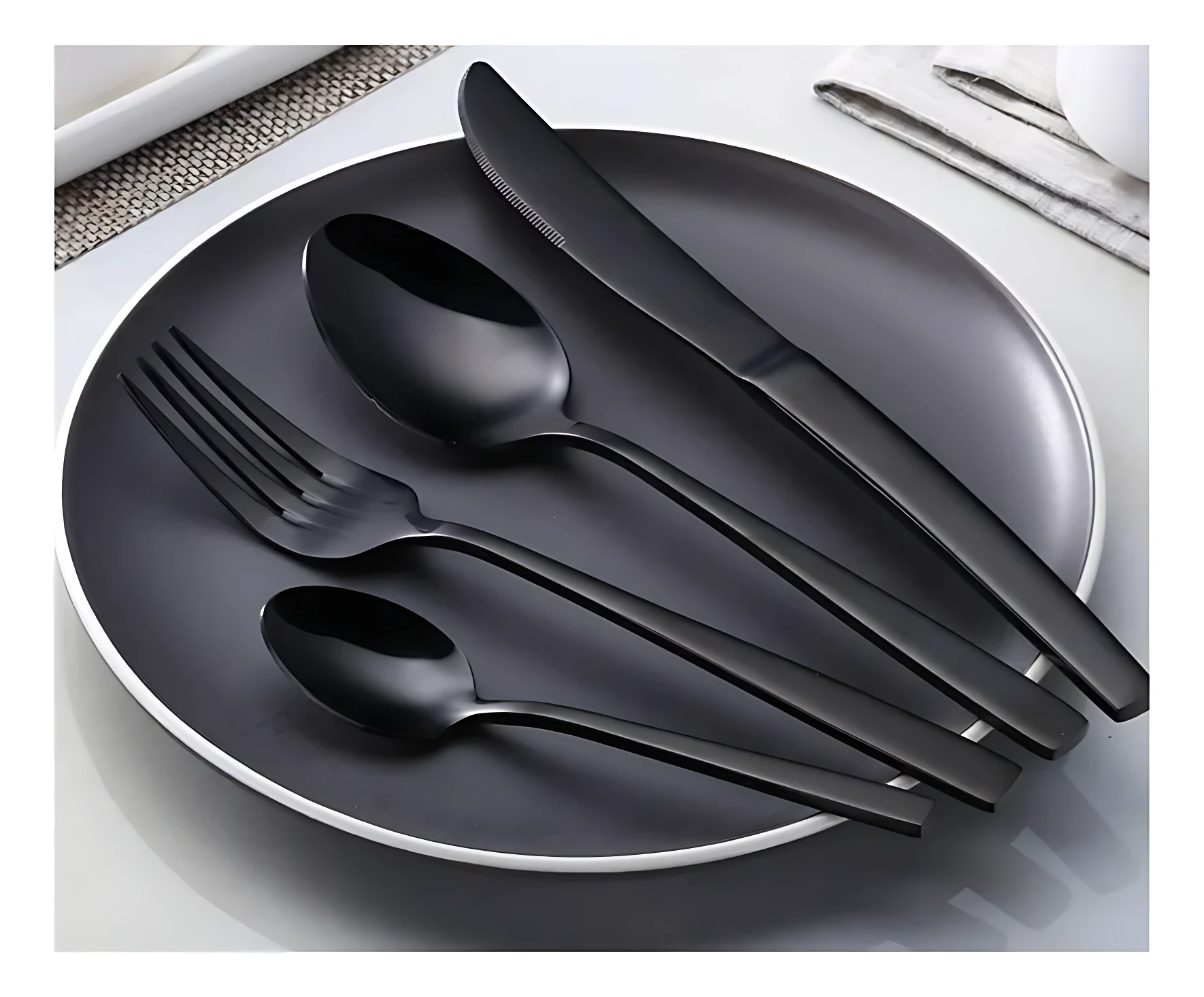 Juego de cubiertos negro mate sobre plato, incluye tenedor, cuchara y cuchillo, vista cenital.