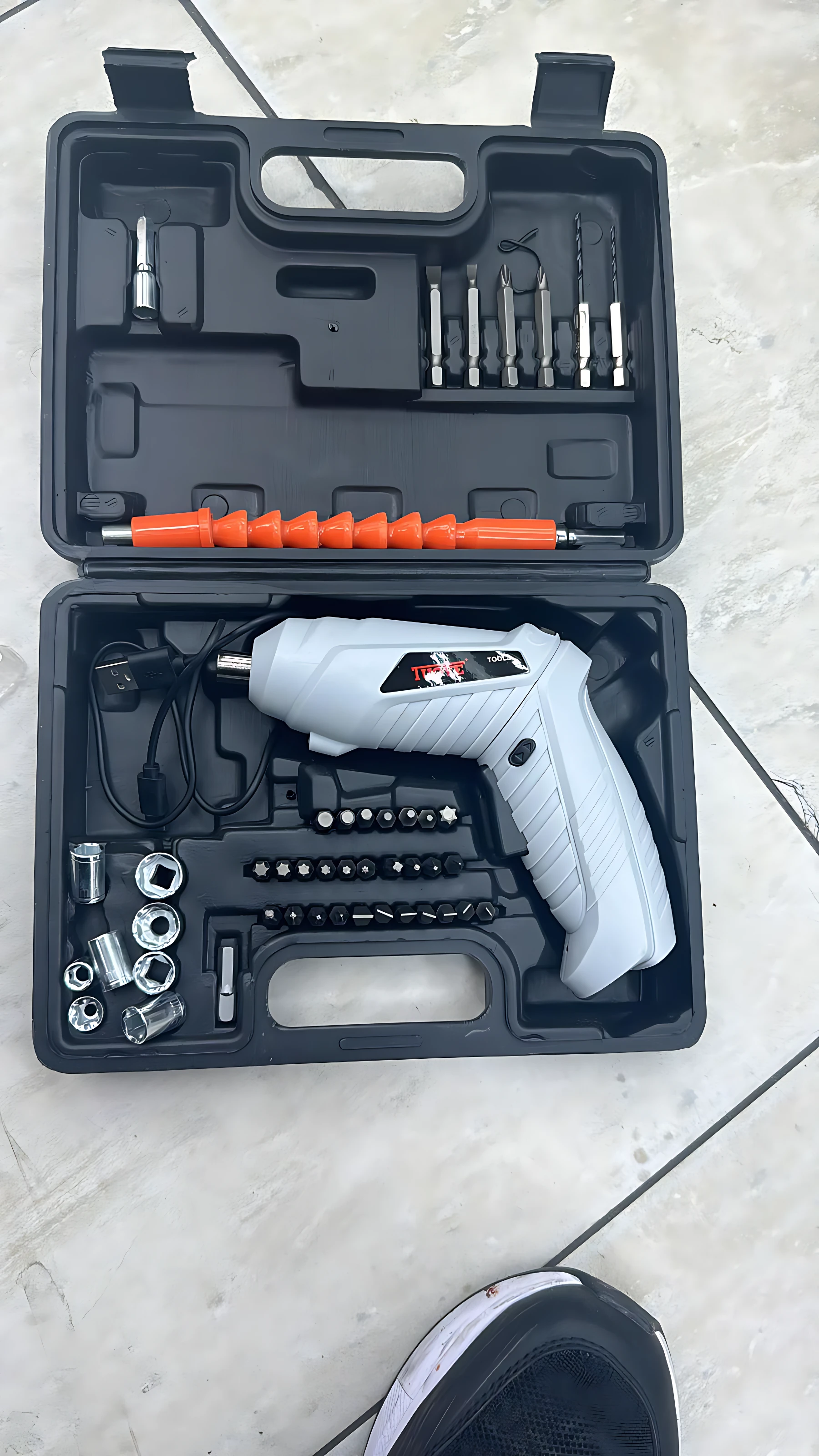 Destornillador inalámbrico recargable blanco con caja negra abierta, mostrando accesorios organizados: brocas, puntas, adaptadores y taladro de rosca naranja.