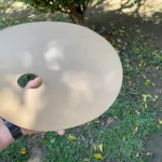 Paleta de madera beige con orificio central para el pulgar, sostenida en mano sobre césped con hojas dispersas.
