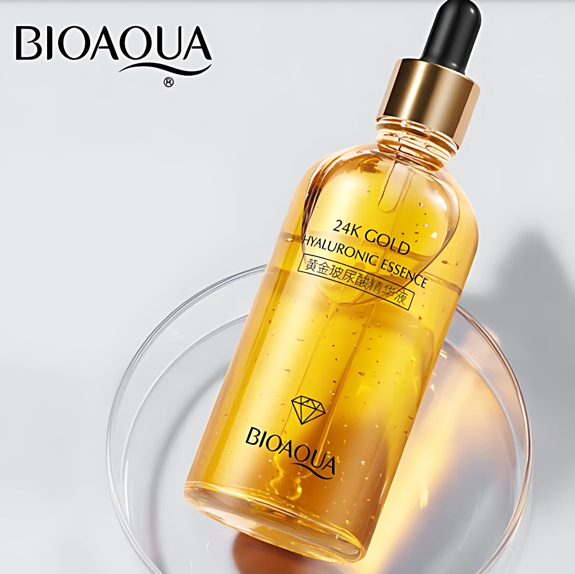 BIOAQUA, sérum de 24K Gold Hyaluronic Essence en frasco de vidrio transparente con líquido dorado y gotas visibles, sobre superficie curva reflectante.
