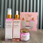 Kit de cuidado corporal Truly con dos aceites después de afeitado, un bálsamo corporal y su caja rosa, sobre superficie de madera.